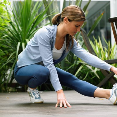 Woman wearing running clothes performing leg stretch in garden