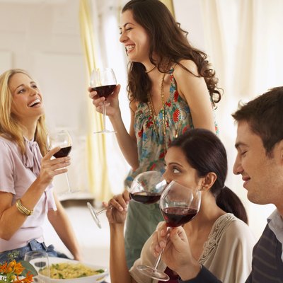 Three young women and young man drinking red wine, two women laughing