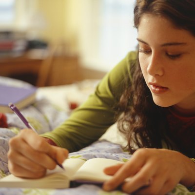 Teenage girl (16-17) lying on bed, writing, close-up