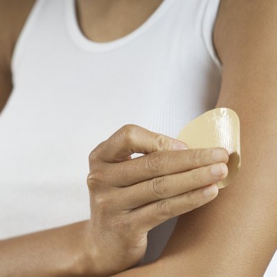 Woman applying patch to arm, mid section