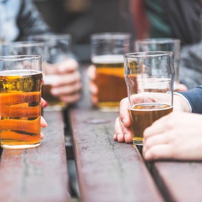 Hands holding glasses with beer on a table at a pub.