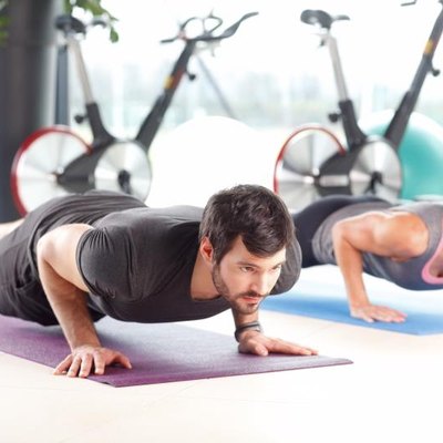Portrait of personal trainer woman and man doing push ups at the gym.