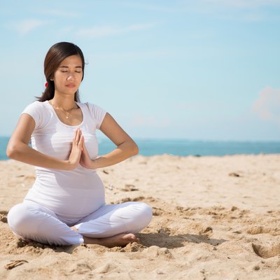 pregnant woman doing yoga in the beach