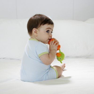 Baby girl (15-18 months) sitting on bed, biting toy