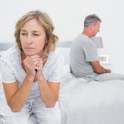 Unhappy couple sitting on different sides of bed having a dispute