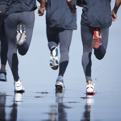 Four men jogging on beach, low section, rear view