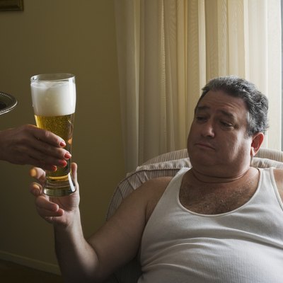 Mature overweight man sitting in armchair, maid (close-up of hand) serving glass of beer