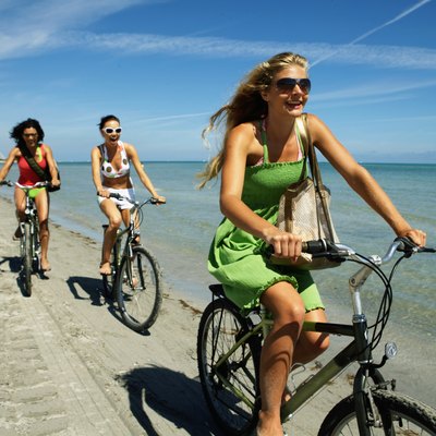 Three young women riding bicycles on beach, smiling