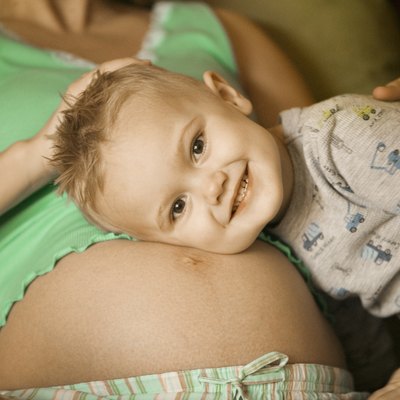 Pregnant mother lying in sitting room, cuddling young son to stomach, close-up