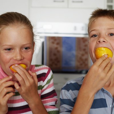 Twin brother and sister (10-12) with oranges in mouths, close-up