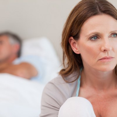 Sad woman on bed with her husband in the background