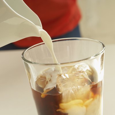 Milk pouring into glass of iced coffee, close up