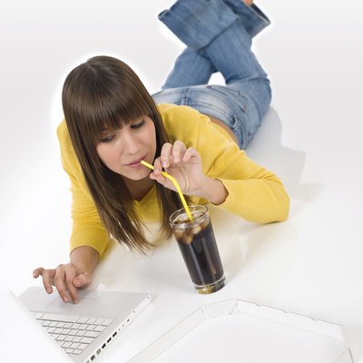 Happy female teenager with laptop lying down drink cola