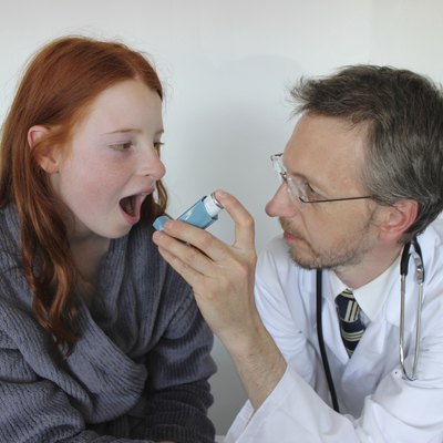 Hospital doctor showing young girl how to use salbutamol inhaler