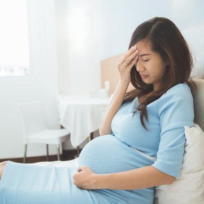 Asian pregnant woman has headache sitting on her bed