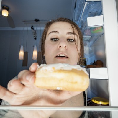 portrait of woman taking donut from fridge