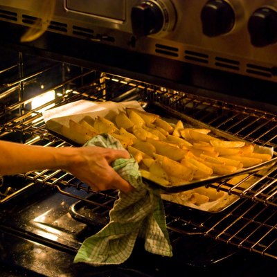 Woman lifting a tray of potato wedges into oven