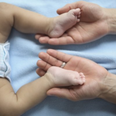 Close-up of a person's hands holding a baby's legs