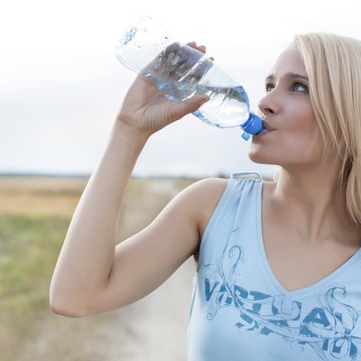 Beautiful woman drinking water from bottle while standing on field
