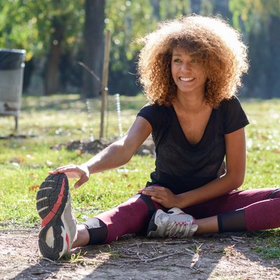 Fitness black woman runner stretching legs after run