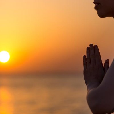 Profile of serene young woman relaxing on the beach, meditating with hands in Namaste gesture at sunset or sunrise, close up