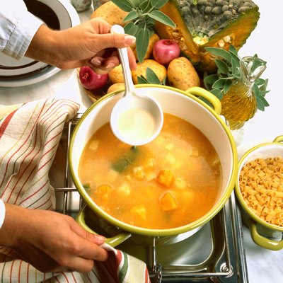 close-up of a hand stirring a bowl of soup cooking on a stove
