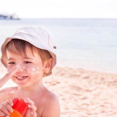 Hand of mother applying suncream to her son on beach.