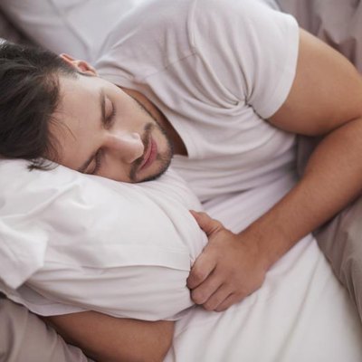 A tired man rests in the bed.