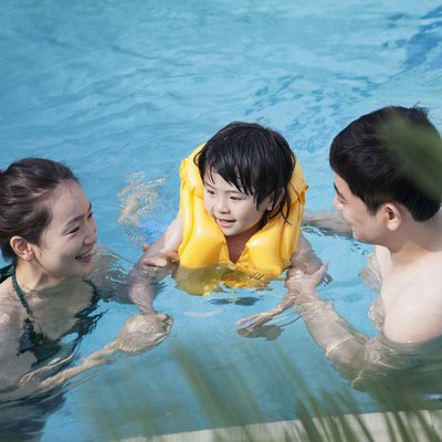 Happy smiling family teaching son how to swim in the pool