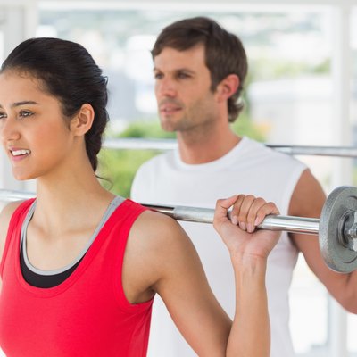 Fit young couple lifting barbells in gym