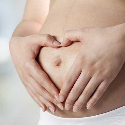 Young pregnant woman making heart shape on belly, close up