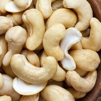 Wooden bowl of cashew nuts from above. On dark wood.
