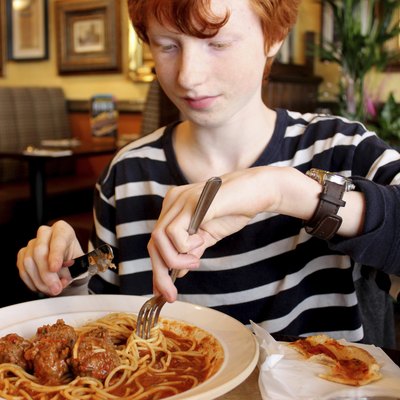 Image of boy eating spaghetti meatballs pasta in Italian restaurant