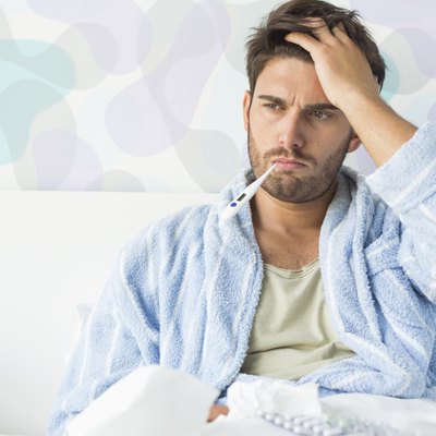 Sick man with thermometer in mouth sitting on bed