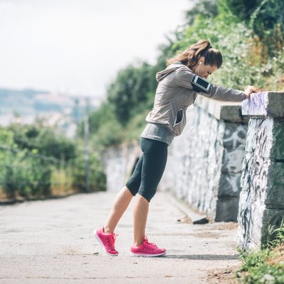 Woman runner stretching against rock wall