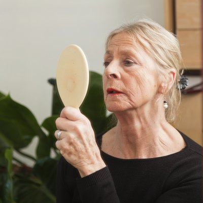 Good looking senior woman doing make-up in front of mirror.