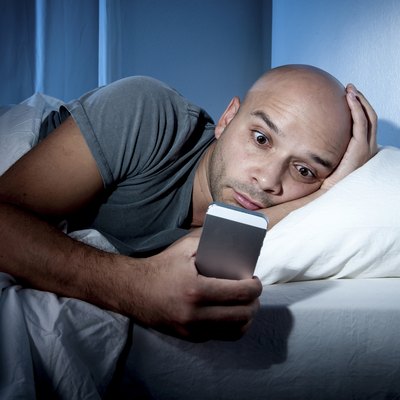 young cell phone addict man in bed using smartphone
