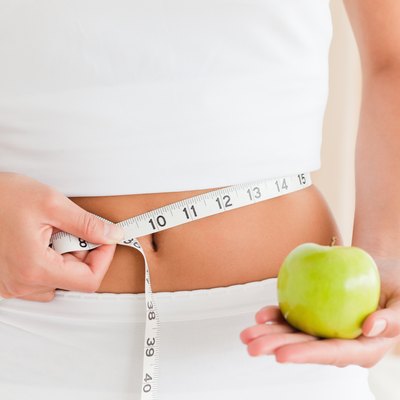woman measuring her waist while holding an apple