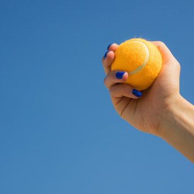 Female hand holds a bright orange tennis ball