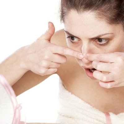 young woman squeeze her acne in front of the mirror