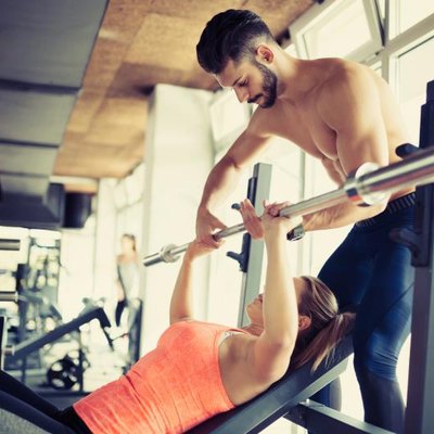 A personal trainer assists a woman with her bench press at the gym.
