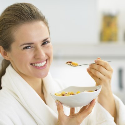 happy young woman eating muesli in kitchen