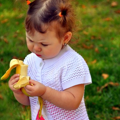 little girl eating a banana in summer outdoors