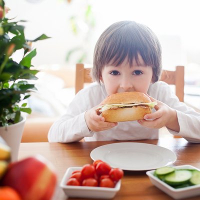 Beautiful little boy, eating sandwich at home, vegetables on the