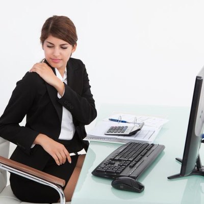 Young businesswoman having shoulder pain while working at computer desk in office