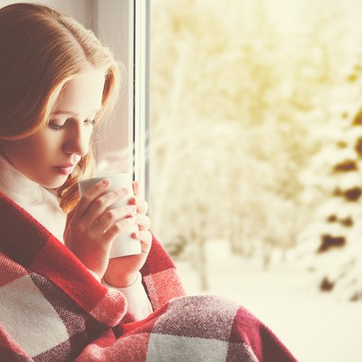Pensive sad girl with a warming drink looking ou window