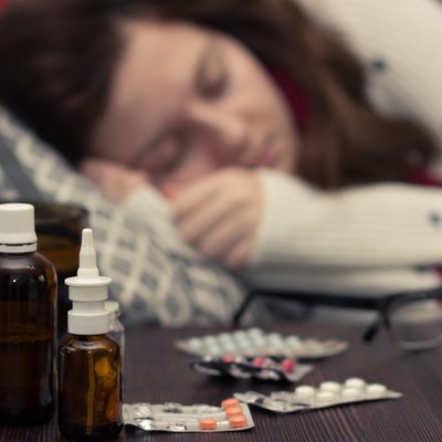 sick woman sleeping in bed next to pills and drugs