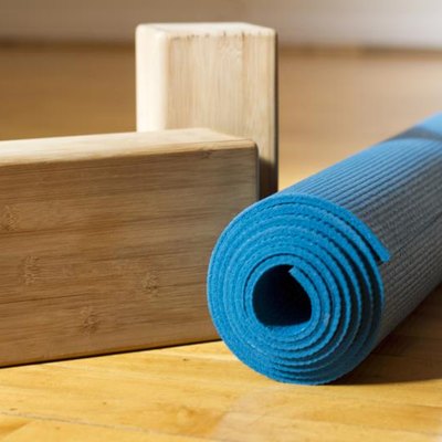 A blue yoga mat with two wooden yoga blocks sit on a wooden yoga studio floor before class.