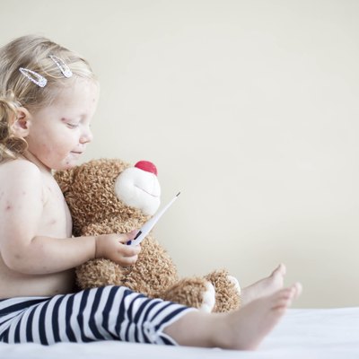 Sick girl is sitting on the bed with teddy-bear