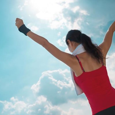 Active woman with outstretched arms against the blue sky, rear view